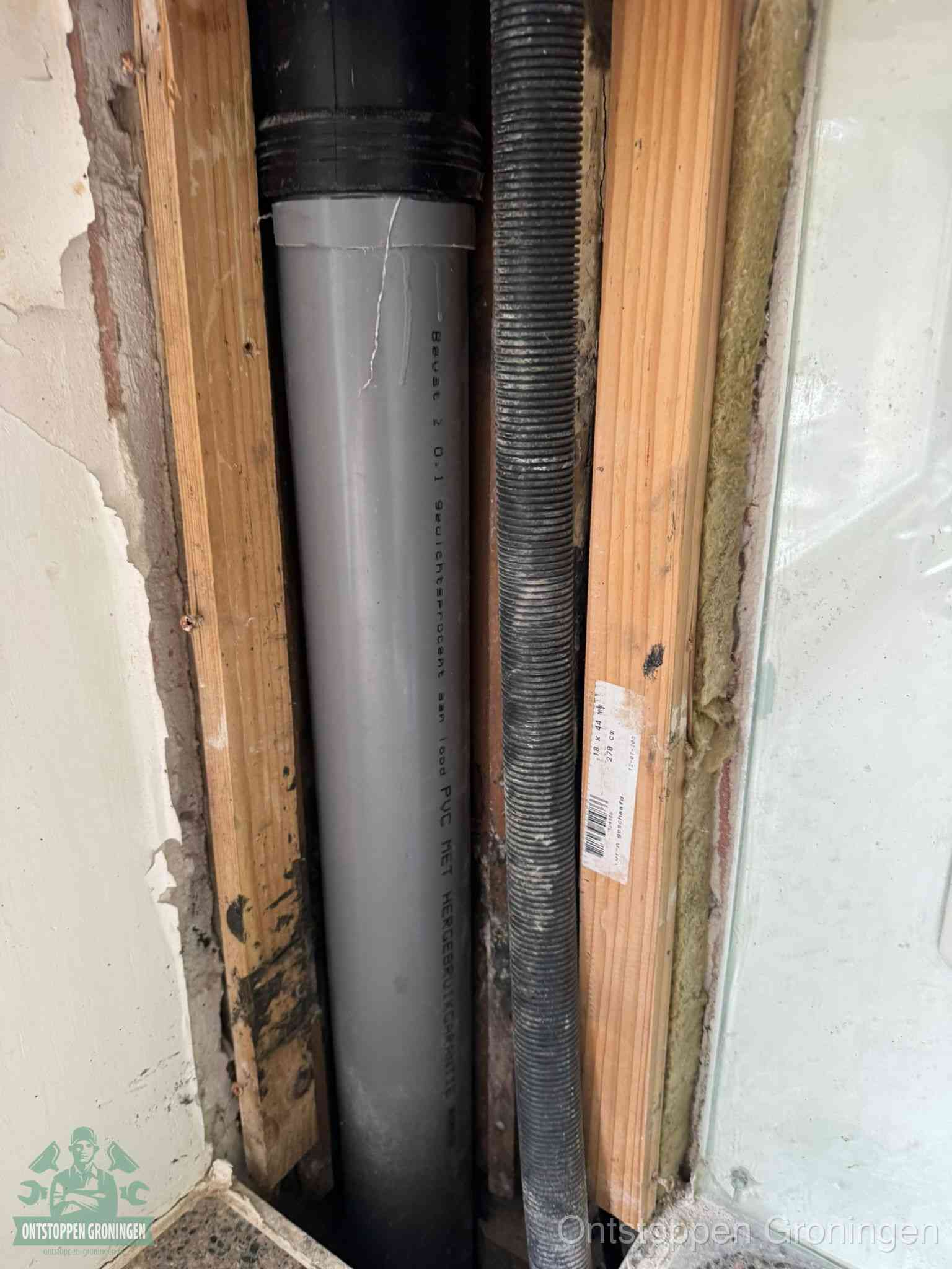 Een grijze PVC-afvoerbuis met een flexibele ribbelslang in een open wandconstructie, een verwaarloosde afvoer die te lang is blijven zitten in Groningen