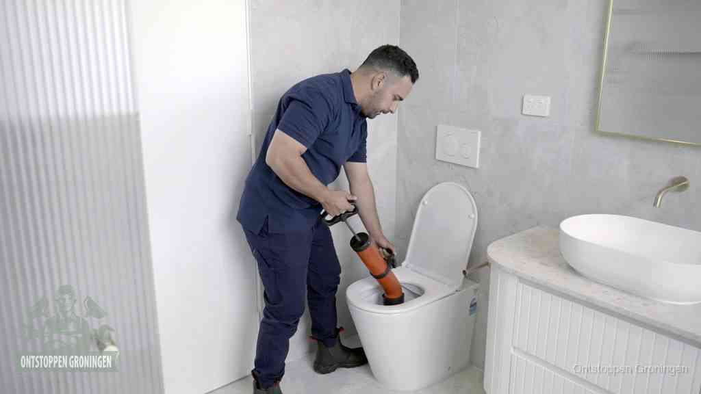 Een monteur buigt over een wandcloset en duwt met de hand een persluchtontstopper in de toiletpot om de verstopping handmatig los te maken in Groningen