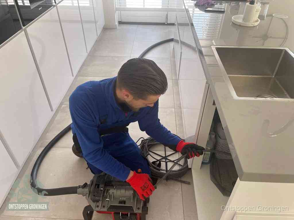 Een monteur ontstopt de keukenafvoer onder de spoelbak met een elektrische veermachine in Groningen