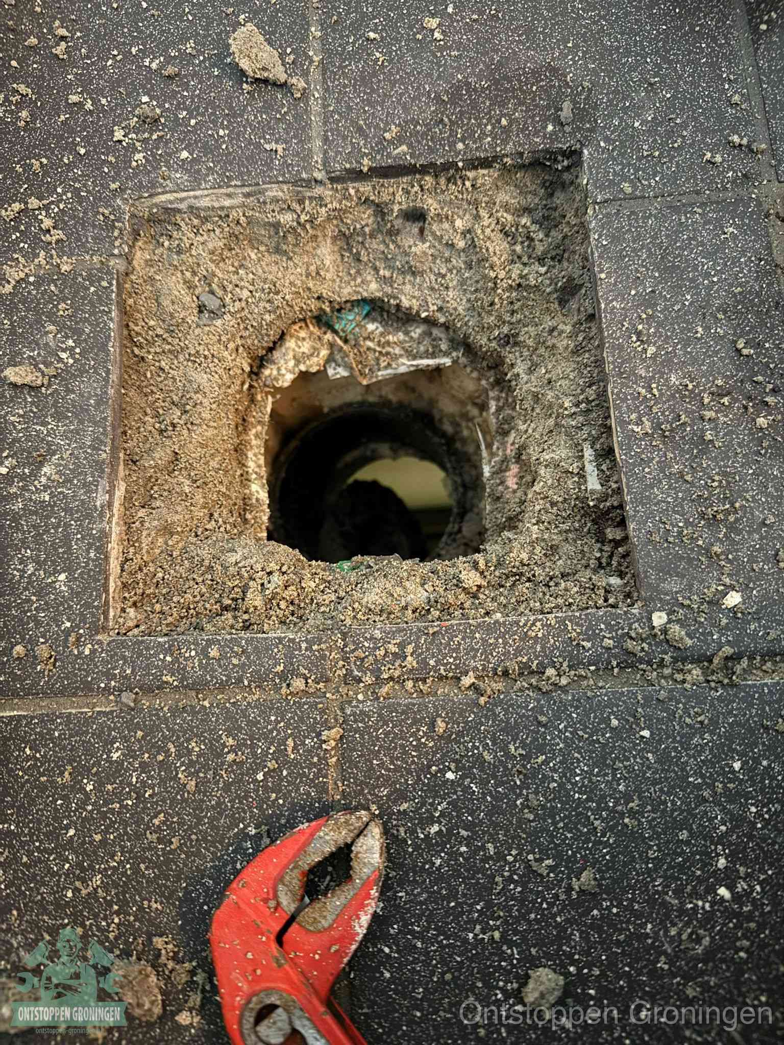 Een geopend rioolputje in een betontegelvloer met losgemaakt rooster en een zichtbare ronde afvoerbuis, het achterhalen waar de afvoerverstopping zit in Groningen