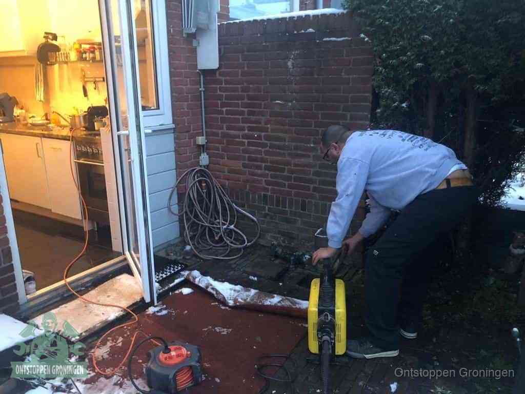 Een monteur werkt buiten bij een open riool-/grondput met een elektrische ontstoppingsmachine om een verborgen afvoerprobleem op te sporen in Groningen