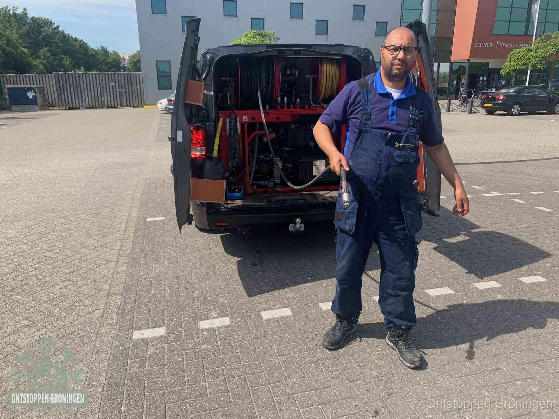 Een monteur bij zijn bestelbus met een hogedruk- en rioolreinigingsunit, klaar om de oorzaak van terugkerende wc-verstoppingen aan te pakken in Groningen