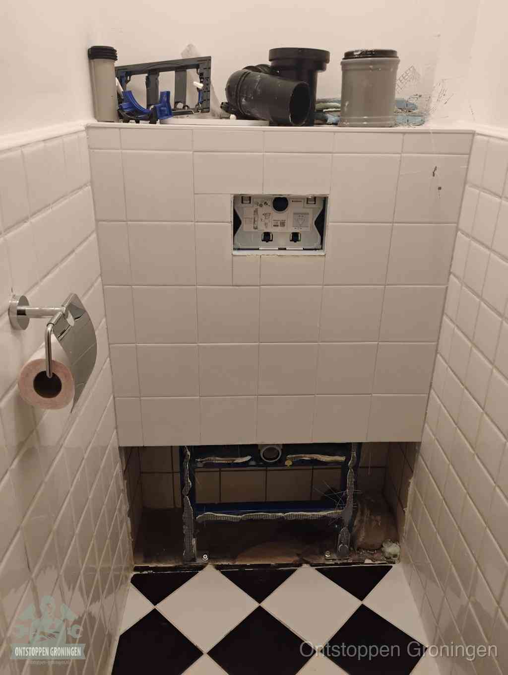 Een toiletruimte waar het hangtoilet en de inbouwreservoir-onderdelen zijn vrijgelegd voor onderhoud, periodiek nazicht voorkomt een wc-verstopping in Groningen