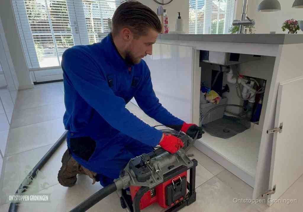Een monteur voert een professionele elektrische ontstoppingsmachine in de afvoer onder de spoelbak tijdens het gootsteen ontstoppen in Groningen